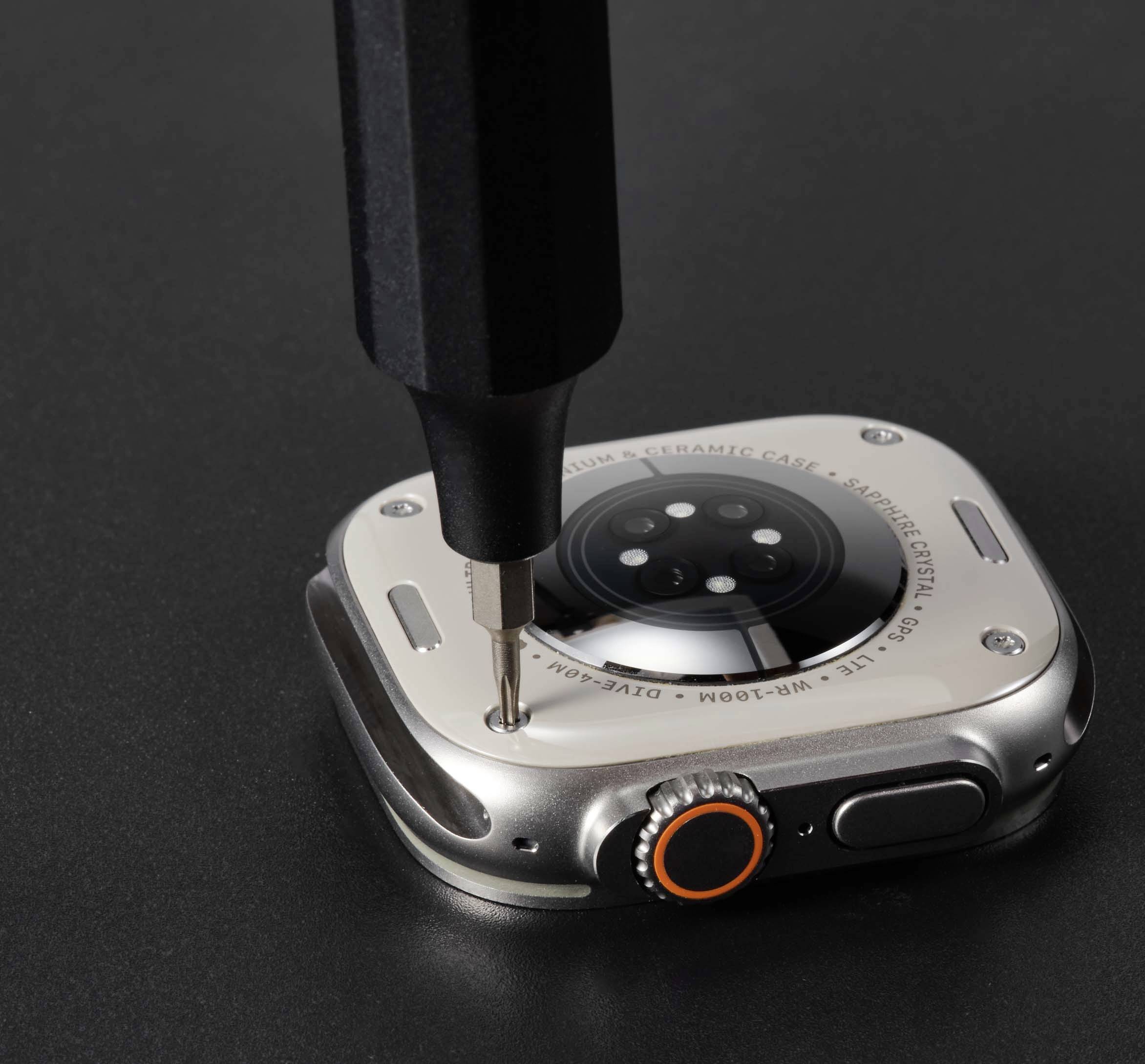 Ura se odpira s izvijačem. Vidna je njena zadnja stran, ležeča na temnem ozadju.