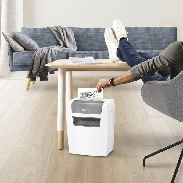 Mož sedi z nogami na mizi in sproščeno bere dokument. Na prvem planu je uničevalec dokumentov, označen z napisom "ZASEBNO".