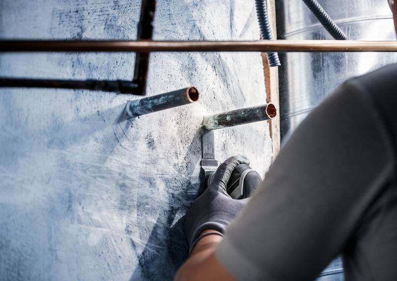 Inštalater dela s kovinskimi cevmi v stavbi. Nosi rokavice in uporablja orodje za obdelavo cevi.