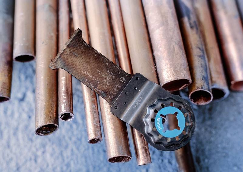 Na mizi ležijo različne bakrene cevi, zraven pa orodje za rezanje ali obdelavo cevi.