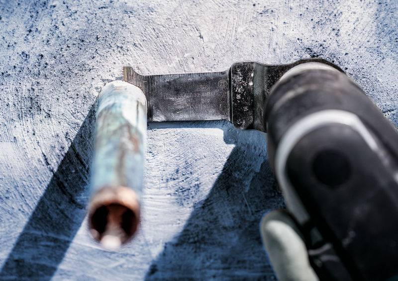 'Roka drži orodje, ki reže kovinsko palico. Prašna podlaga in močna senca poudarjata delovno okolje.'