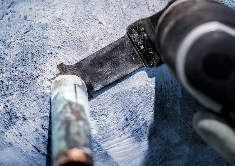 Bližnji posnetek rezalnega orodja, ki reže kovinsko cev. Grobo modra površina v ozadju.