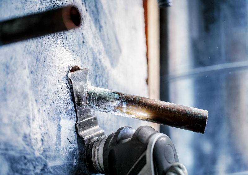 Instalater spaja bakreno cev na stenski povezavi. Medtem ko se kovina segreva, okoli letijo iskre.