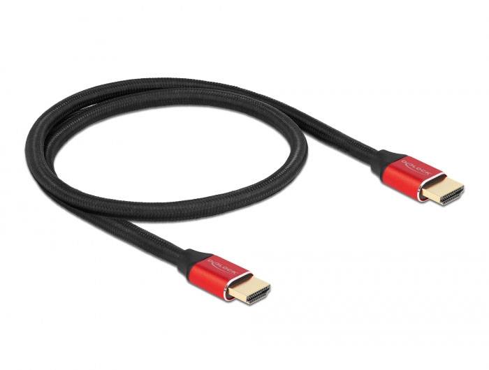 Črn HDMI-kabel z rdečimi vtiči, zložen v zanko, leži pred belo podlago.