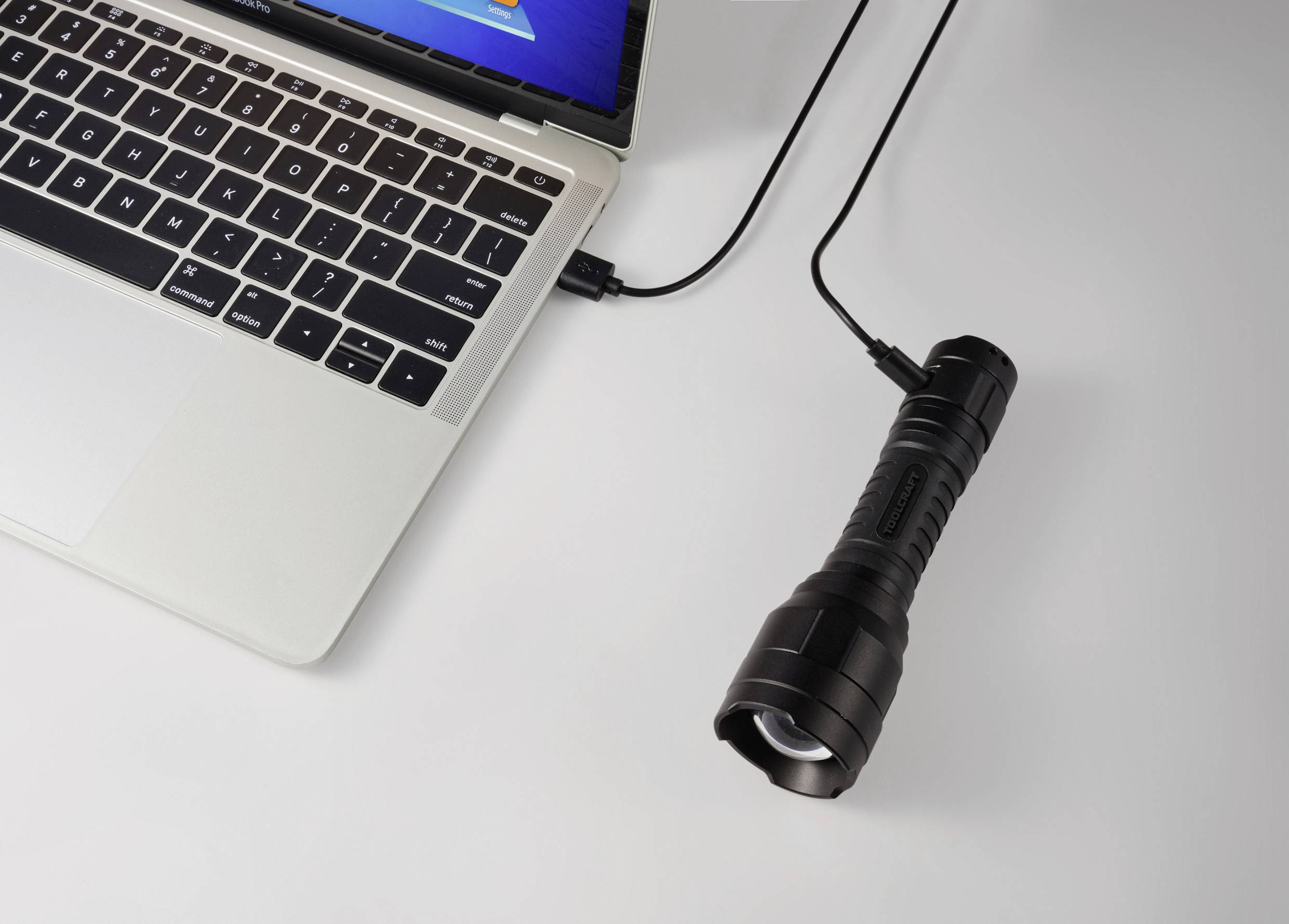 Prenosni računalnik, povezan z baterijsko svetilko prek USB kabla, na mizi.