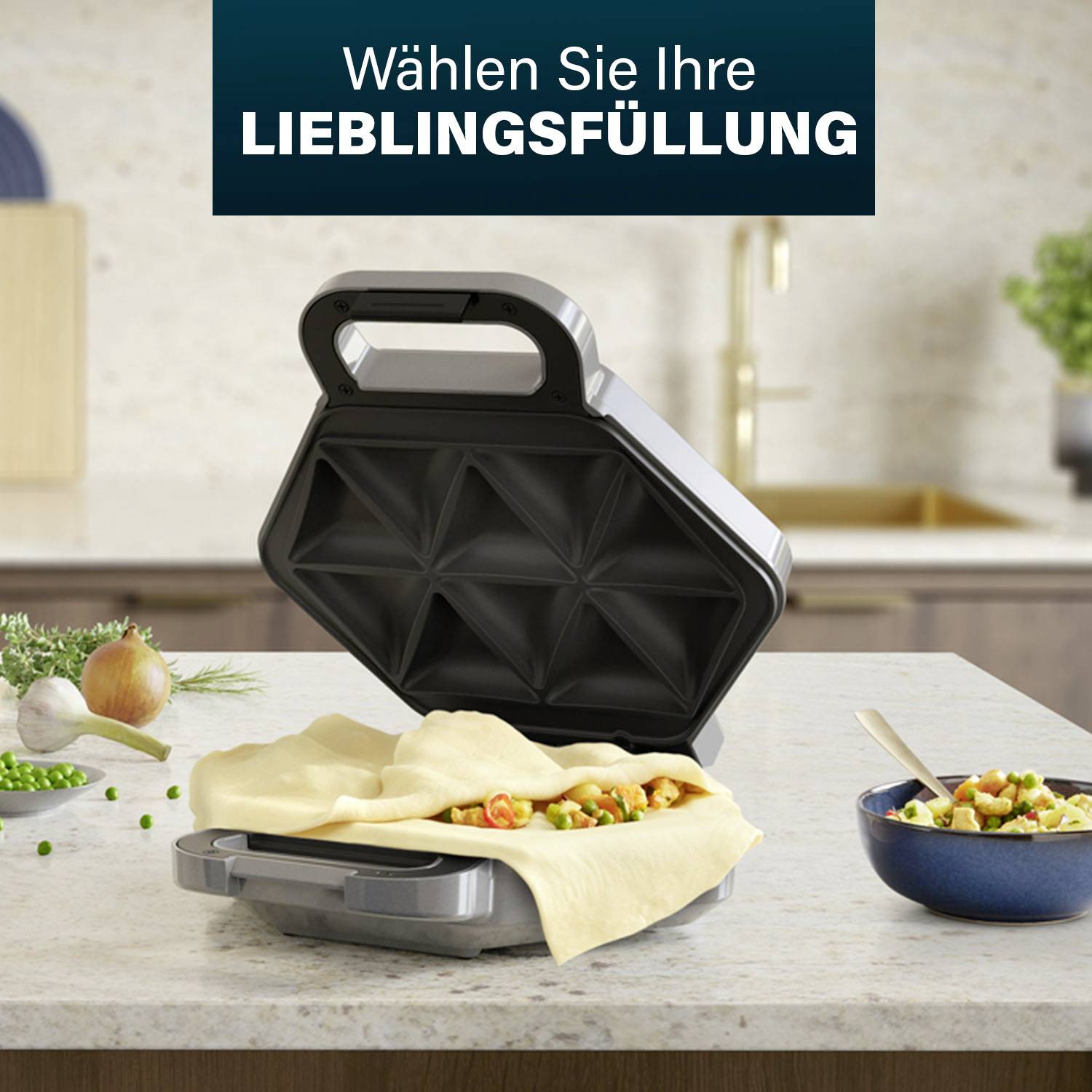 Sendvičnik z odprtim pokrovom, napolnjen s testom in zelenjavo, stoji v kuhinji. Besedilo zgoraj se glasi: 'Izberite svojo najljubšo nadev'.