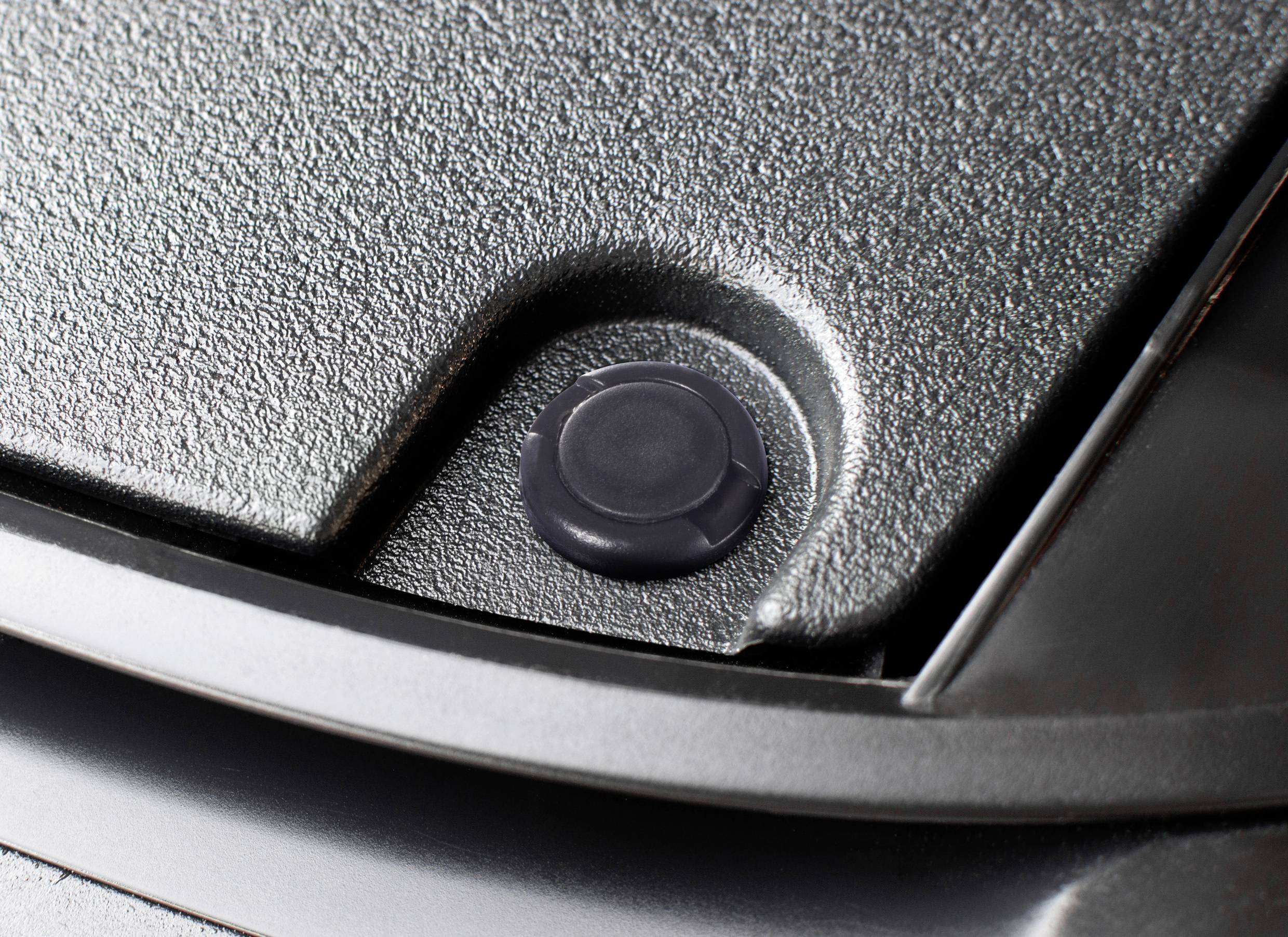 Bližnji posnetek okroglega črnega gumijastega čepa, vstavljenega v vdolbino sive kovinske površine.