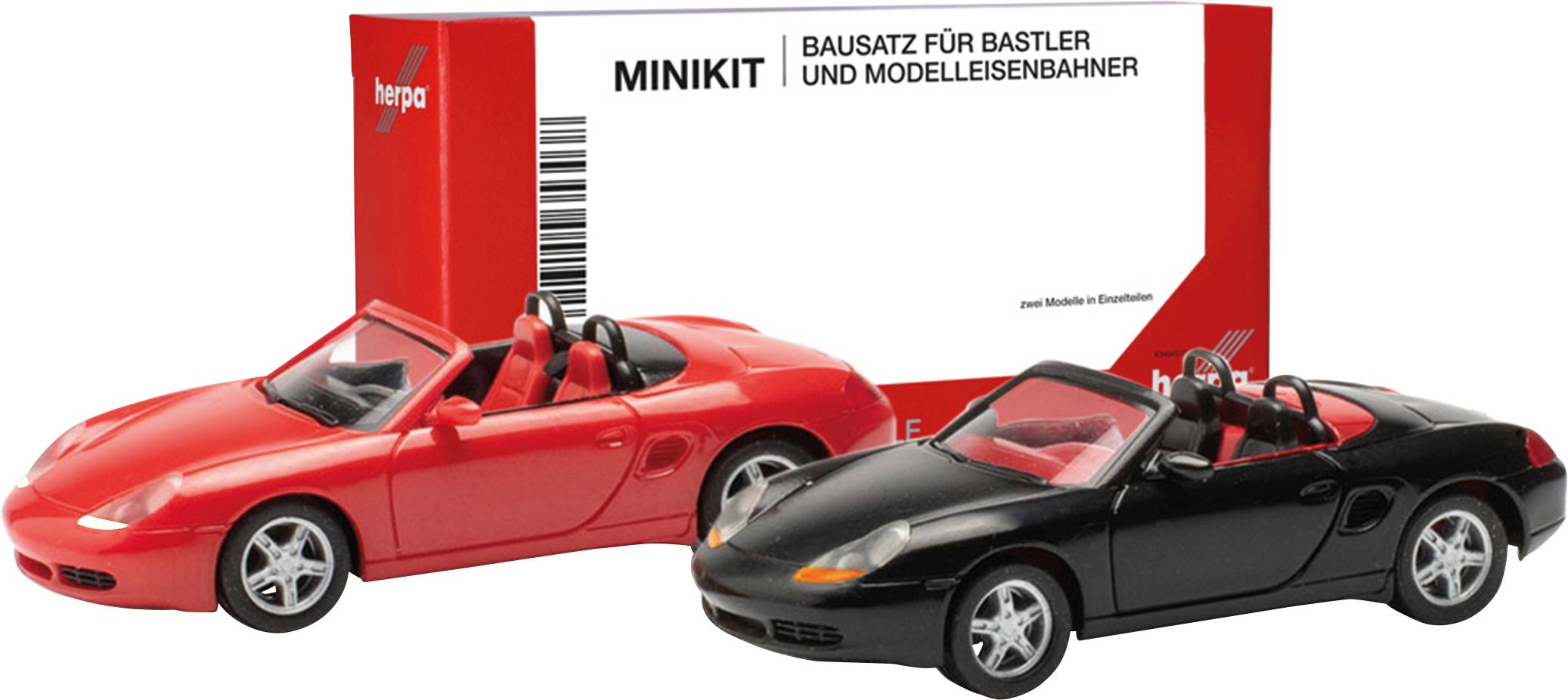 Dva modelna avtomobila, rdeč in črn, pred embalažo z napisom 'Minikit komplet za mojstre in modelne železničarje'.