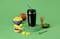 Črn Nutribullet kozarec s slamico na zeleni platformi, obkrožen z narezanim mangom, celo mangovo sadje, matcha praškom in metlico.