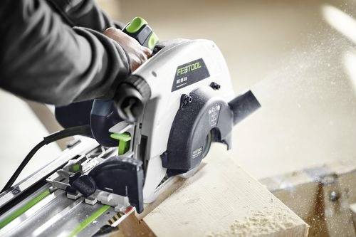 Oseba uporablja krožno žago za rezanje koščka lesa, pri čemer žagovina leti naokrog. Žaga je blagovne znamke 'Festool HK 55'.