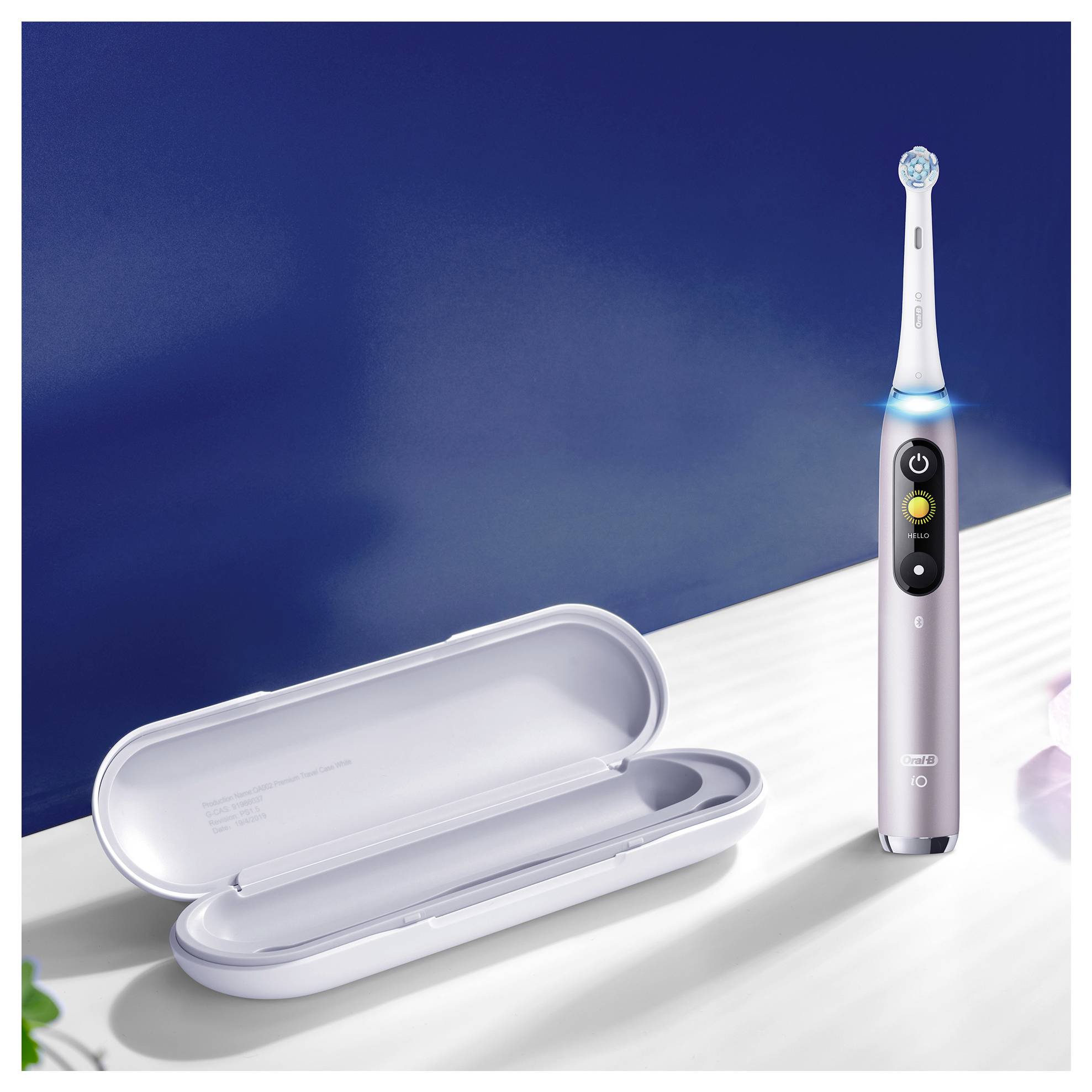 Električna zobna ščetka stoji pokončno poleg odprte potovalne torbice na beli polici pod temno modro steno.