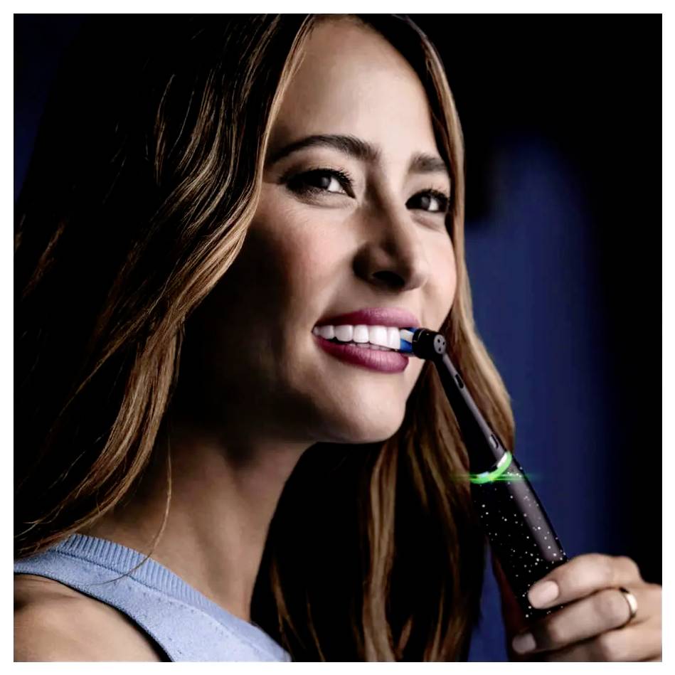 Oseba se nasmihlja med uporabo električne zobne ščetke, pri čemer poudarja zobozdravstveno higieno in nego ustne votline.