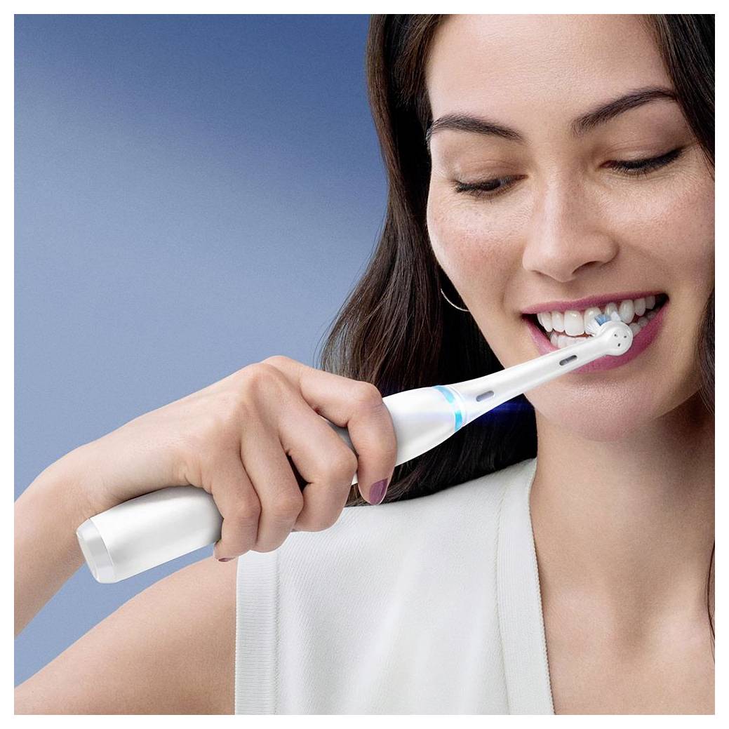 Oseba uporablja električno zobno ščetko in se nasmiha med ščetkanjem zob v dobro osvetljeni sobi.