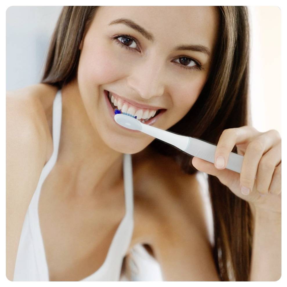 Oseba, ki uporablja električno zobno ščetko, nasmejana, pri čemer poudarja pravilno tehniko ustne higiene.