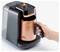 Roka postavi baker obarvano posodo v kompakten kavni aparat z oznako 'OKKA', kar nakazuje, da je pripravljen na kuhanje kave.