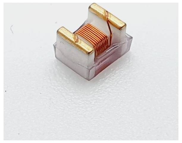 Majhen elektronski komponenten z bakrenimi tuljavami in zlatimi priključki, ki se uporablja za induktivnost v elektronskih vezjih, na beli podlagi.