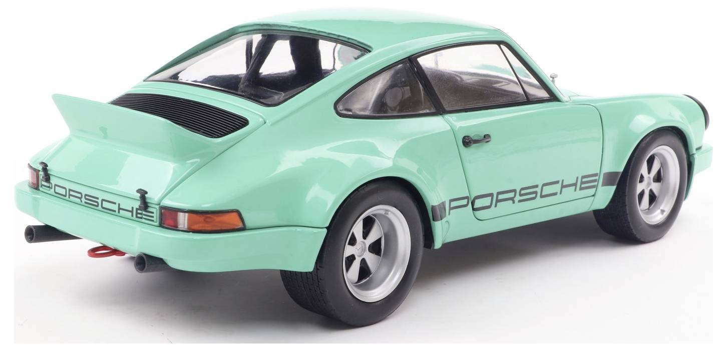 Mintasto zeleni vintage športni avto z elegantno obliko in napisom 'Porsche' na strani, fotografiran pod kotom od zadaj desno.