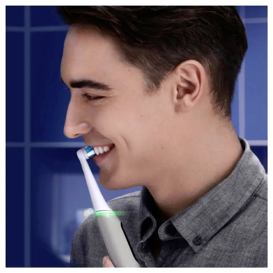 Oseba v profilu se nasmihlja, medtem ko si ščetko za električno čiščenje zob drži ob zobeh in prikazuje uporabo pripomočka za ustno higieno.