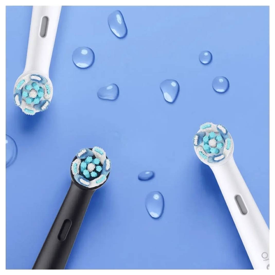 Trije električni nastavki za zobno ščetko, dva bela in en črn, z modrimi ščetinami, razporejeni na modrem ozadju z vodnimi kapljicami.