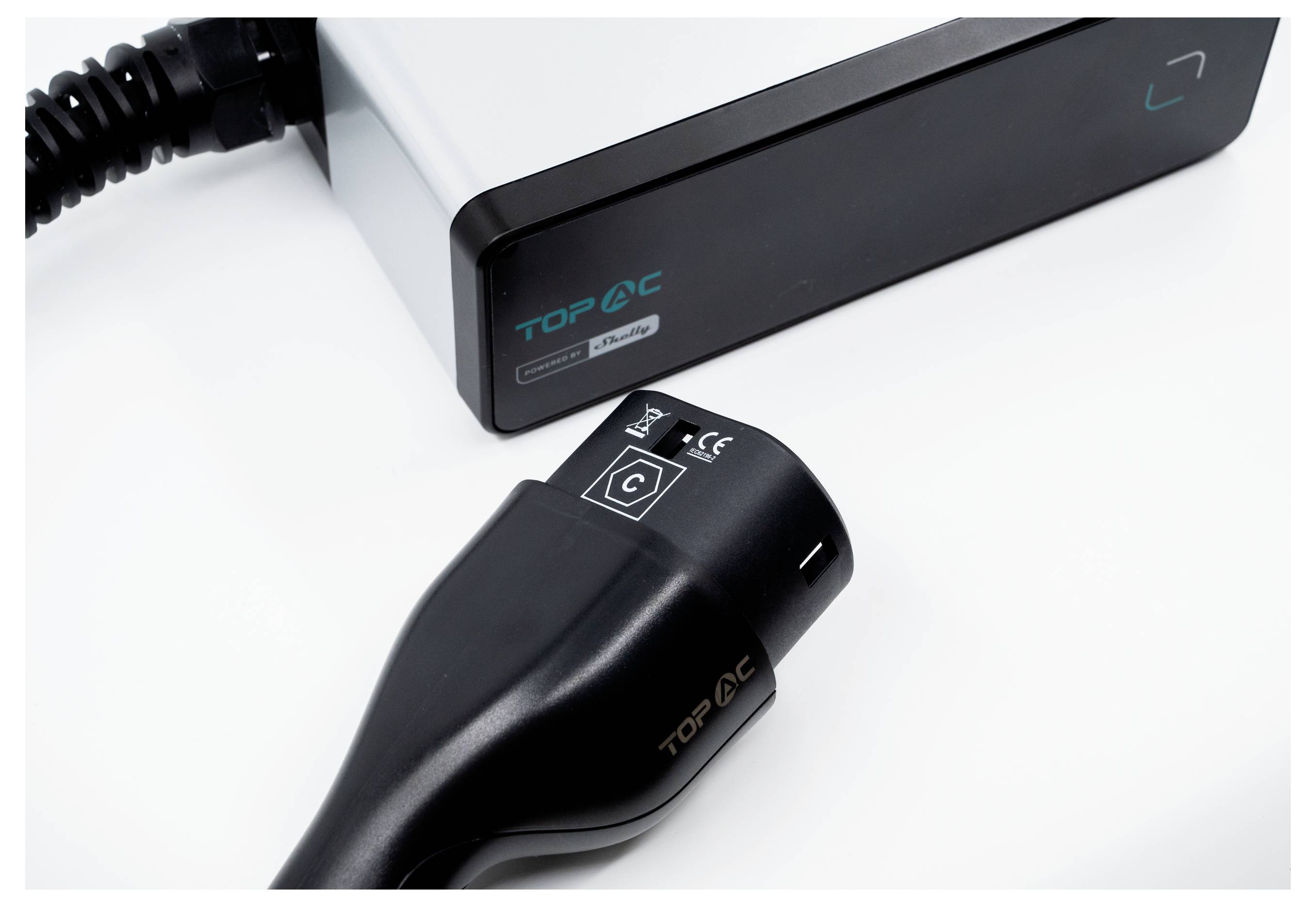 Električni vtič za polnjenje vozila in škatla z oznako 'TOP AC'. Črni vtič je priključen na kovinsko polnilno enoto, na kateri so vidne oznake CE.