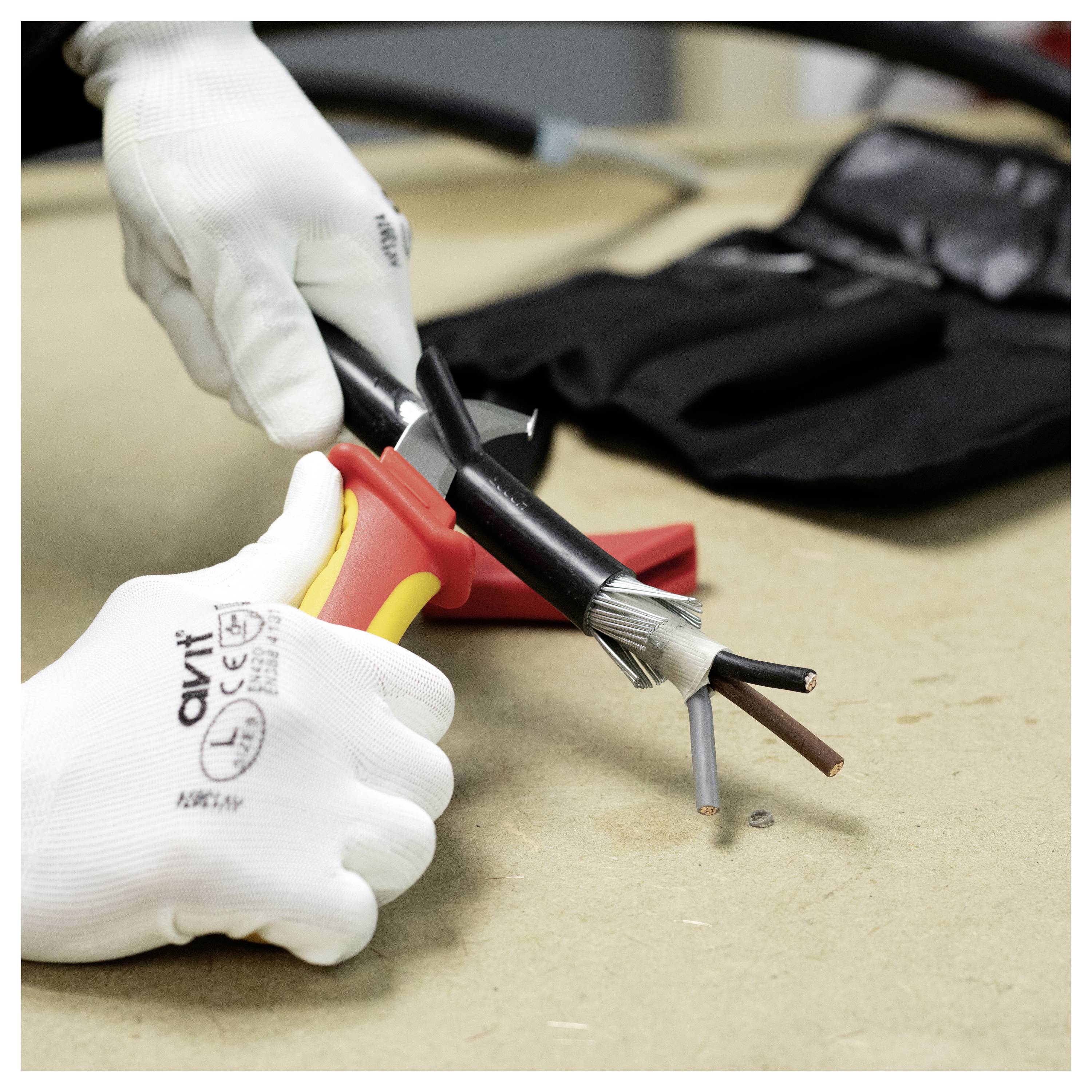 Oseba, ki nosi zaščitne rokavice, uporablja orodje za odstranitev zunanje izolacije električne kable, pri čemer razkrije več žic.