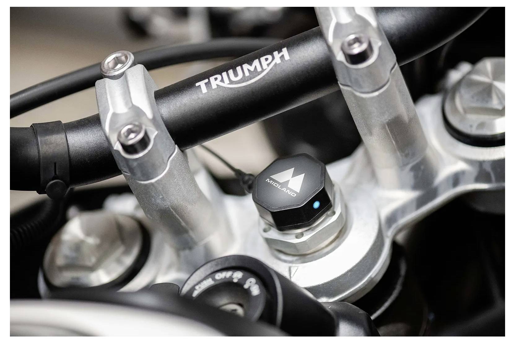 Detaljni pogled na motociklovski upravljač in krmiljenje z logotipom "TRIUMPH" in kovinskimi deli, ki poudarjajo oblikovanje in strukturo.