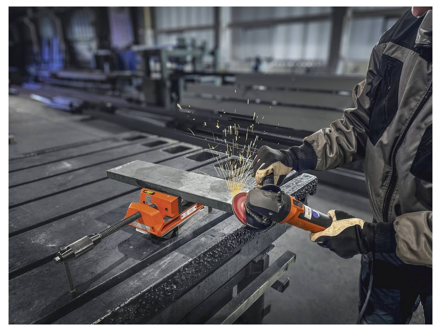 Oseba uporablja ročni brusilnik za rezanje kovinskega drogotina, pritrjenega v delovni stol, medtem ko letijo iskre v industrijskem delavničnem okolju.