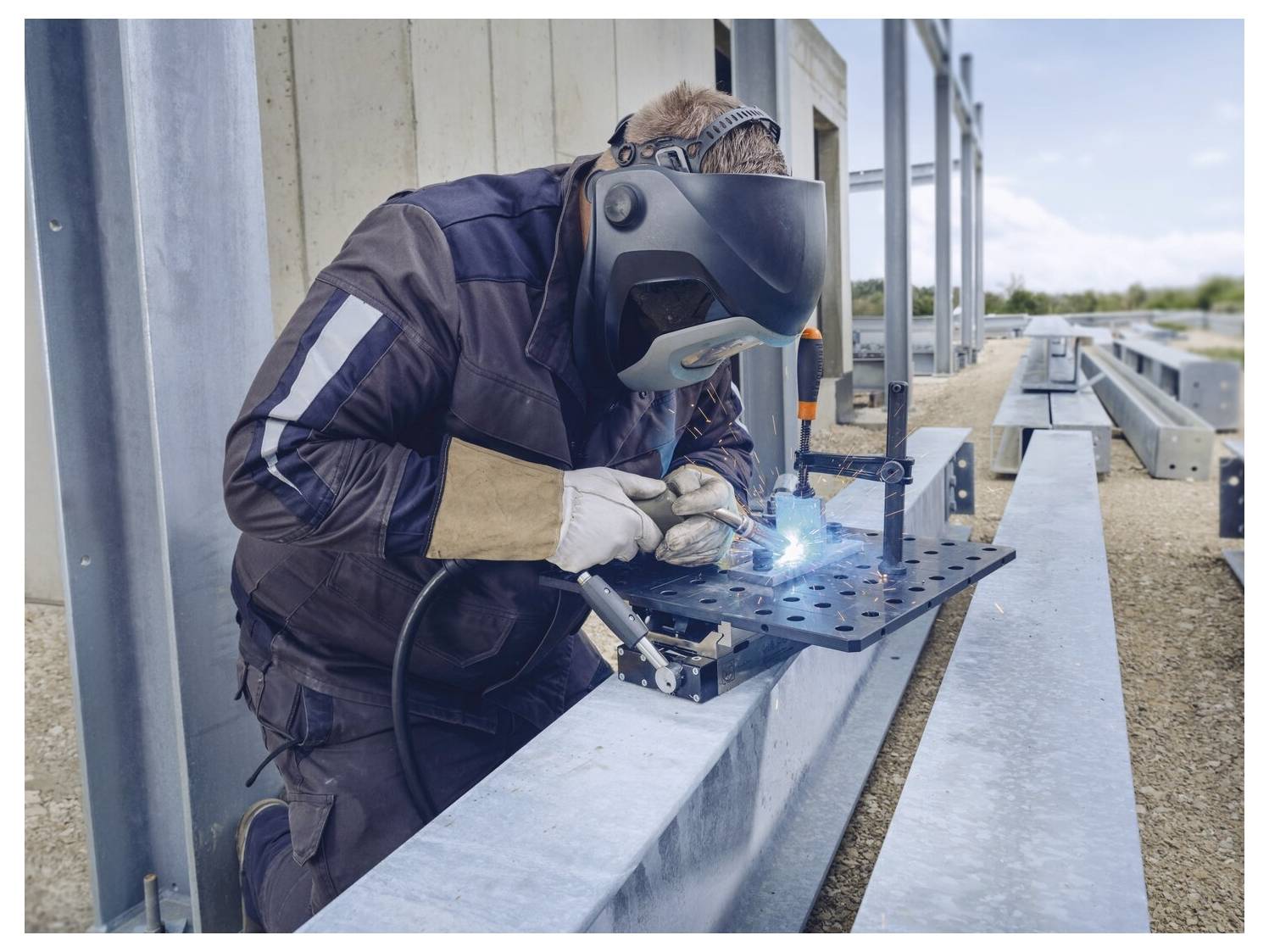 Varilec v zaščitni opremi dela na kovinskih konstrukcijah na prostem, vidna je svetleča modra varilna plamen.