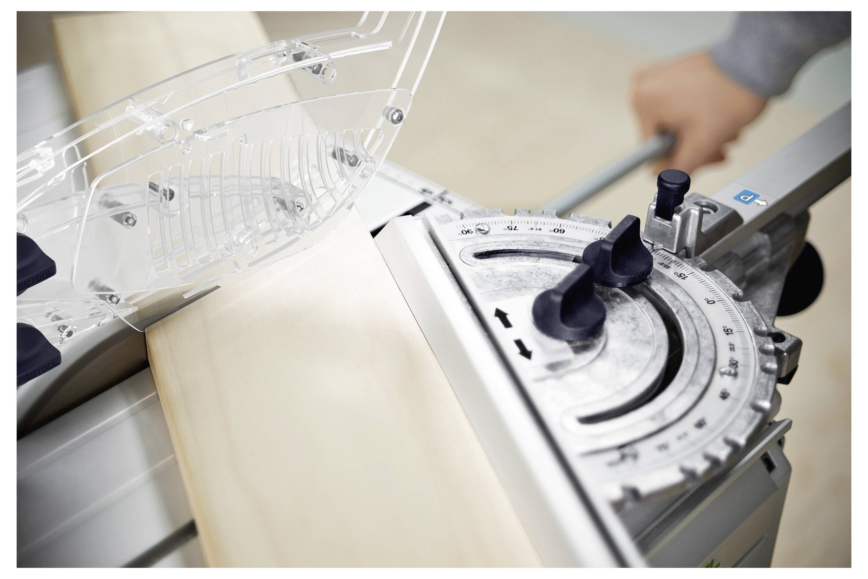 Oseba, ki nastavi krožno žago z leseno desko, postavljeno za rezanje. Žaga ima merilo in zaščitni pokrov za varnost.