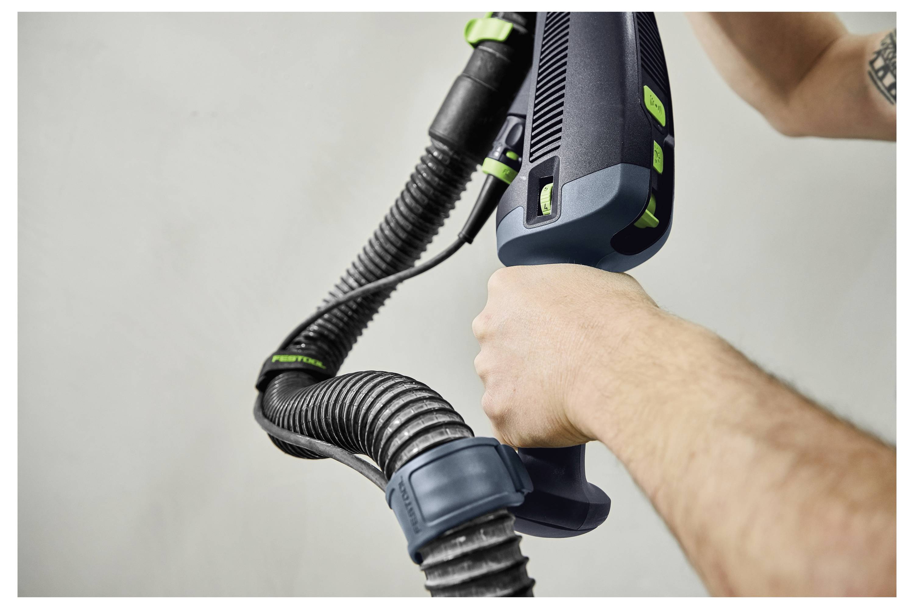 Roke, ki držijo sesalni nastavek in cevi sesalnika, s poudarkom na prijemu in manevski sposobnosti, pred enostavnim ozadjem.