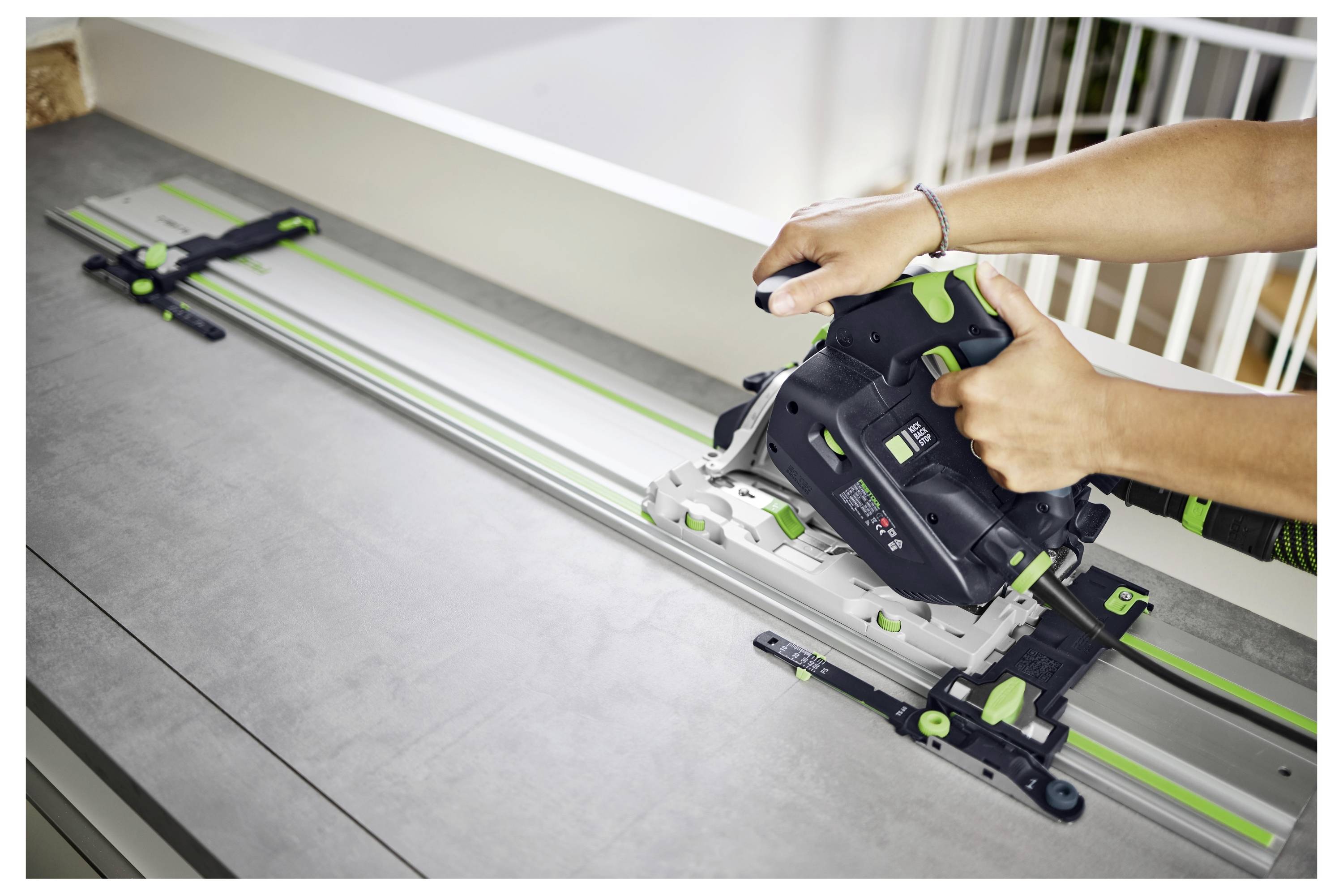 Oseba z ročnim električnim žago na kovinskem vodilu natančno reza plosko površino v zaprtih prostorih.