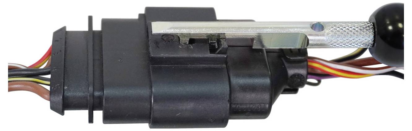 Črni plastičen električni priključek z več barvnimi žicami in kovinskim orodjem, ki je vpeto v njegov zakljepavalki mehanizem.