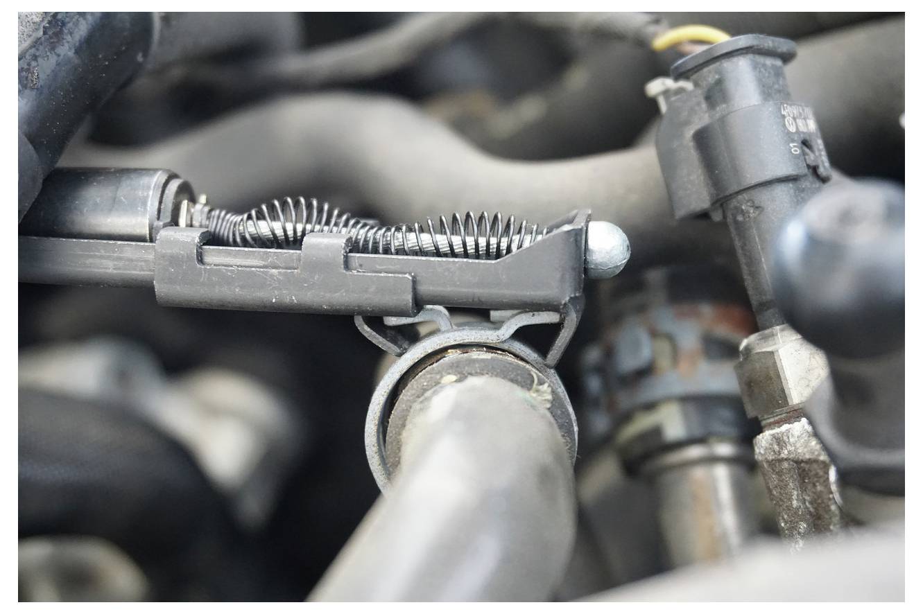 Nahajališčni pogled na komponent avtomobilskega motorja s poudarkom na mehanizmu sponke na vzmet, obdan z različnimi cevmi in spojkami.