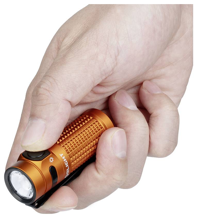 'Roka, ki drži oranžno svetilko, s palcem, ki lebdi nad gumbom za vklop. Svetilka ima teksturirani oprijem in majhno, okroglo lečo.'