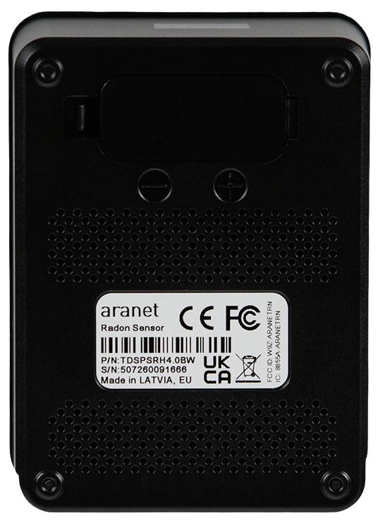 Črn sensor za radon s certifikacijskimi nalepkami, vključno z znaki CE in FCC. Proizvajalec: Aranet. Izdelano v Latviji, EU.