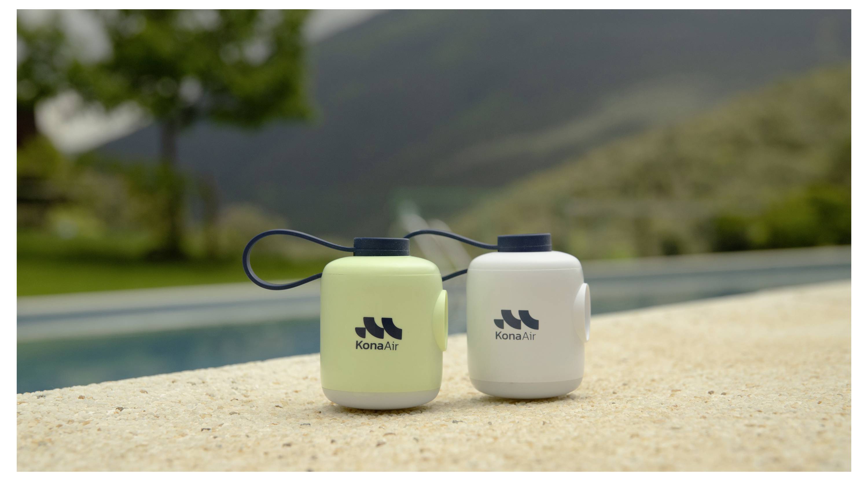 Dve toplotno izolirirani steklenici z znamko KonaAir s prenosnimi zankami stojita na robu bazena, v ozadju pa se vidi zamegljena gorska pokrajina.