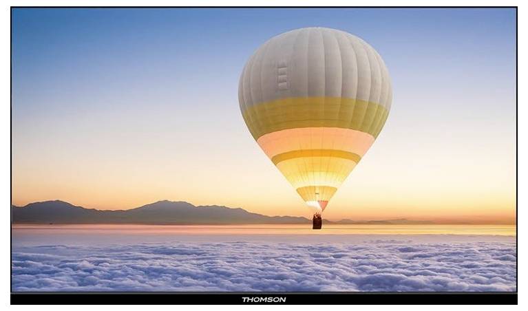 Vroči zračni balon lebdi nad pokrajino, prekrito s oblaki, ob sončnem vzhodu, z oddaljenimi gorami na obzorju.