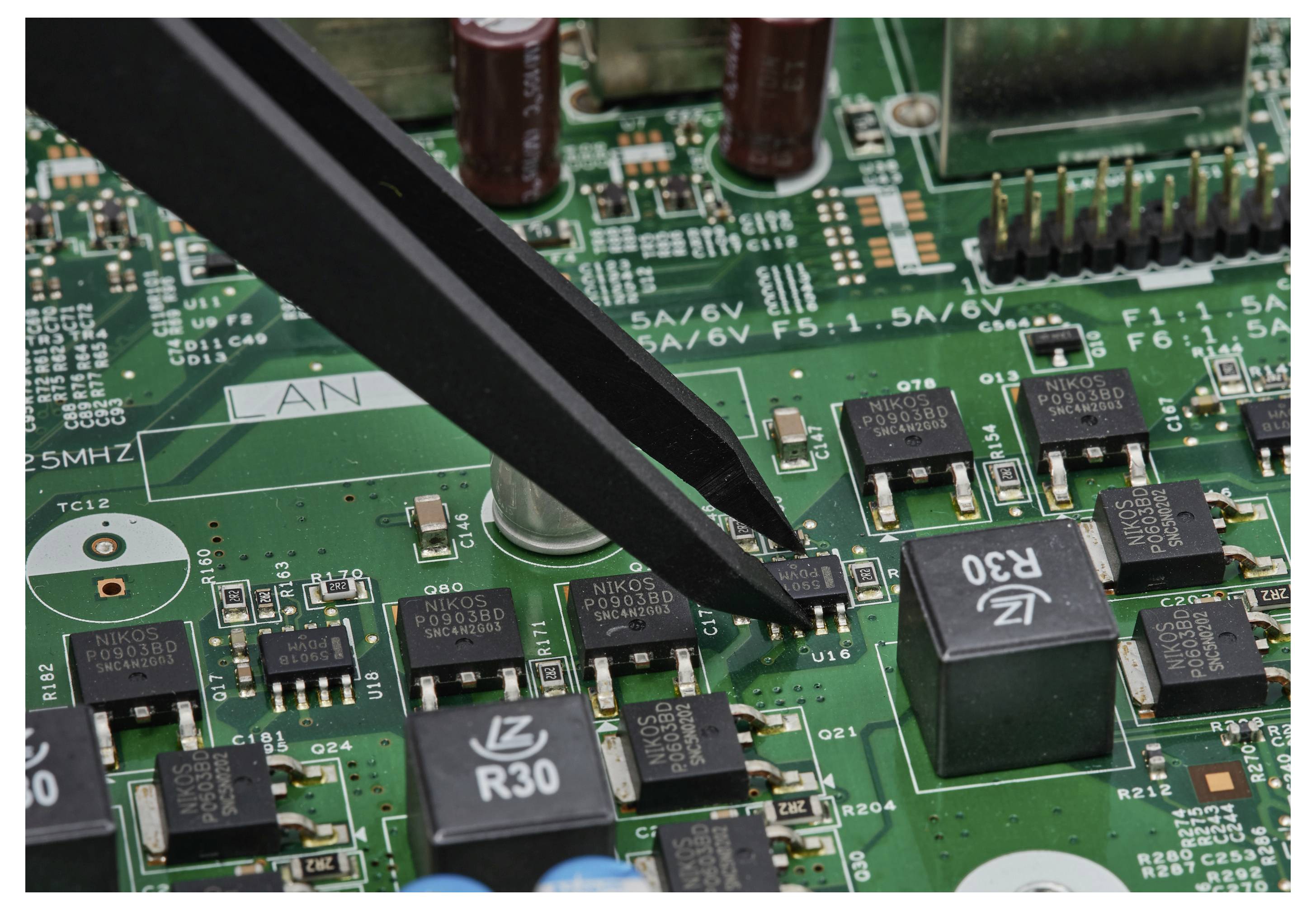 Pincete primejo majhno površinsko komponento na zelenem tisknem vezju med popravilom ali sestavo elektronike.