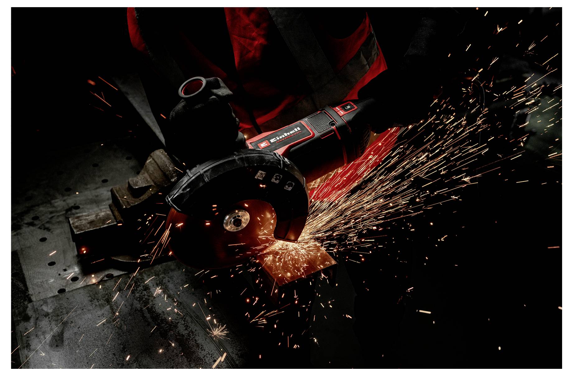 Detajlni posnetek ročnega kotalnega brusilnika, ki reže kovino in pošilja svetlo oranžne iskre čez temno delovno površino.