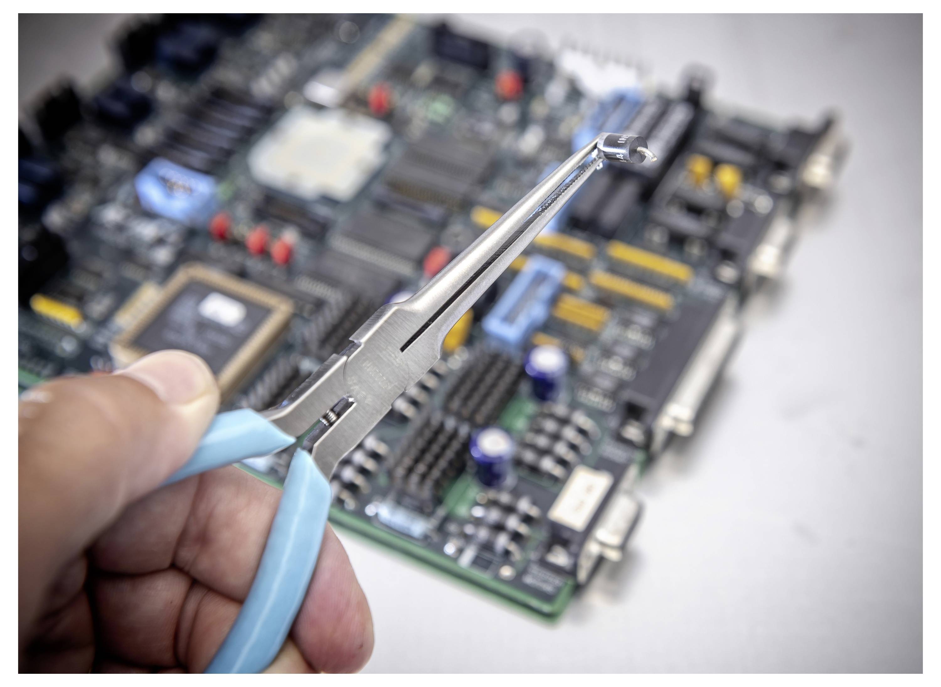Roka drži igličaste klešče nad matično ploščo računalnika, kar nakazuje na popravilo elektronike ali odstranitev komponente.