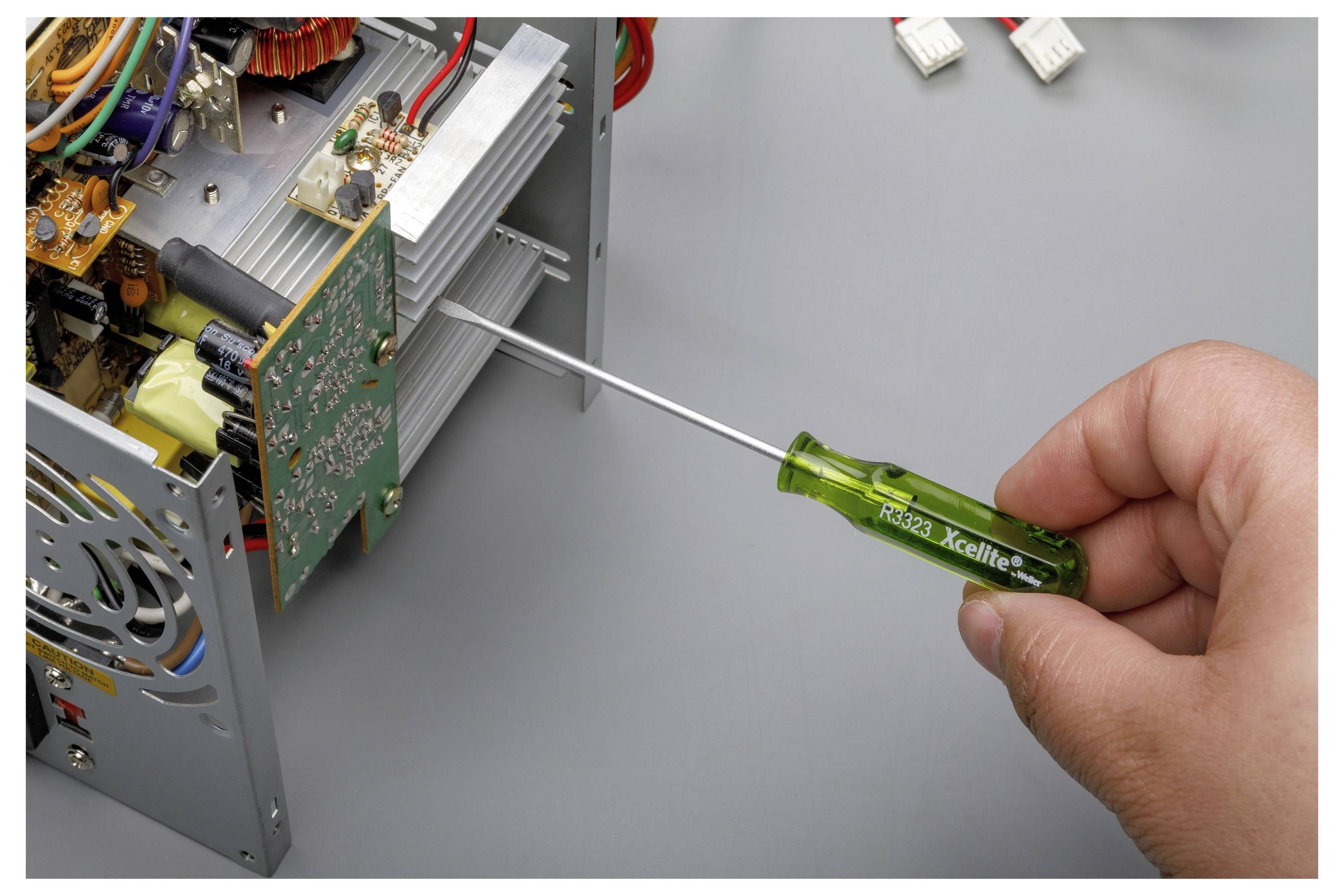Roka, ki uporablja zeleni izvijač za nastavljanje elektronskega vezja v odprti kovinski ohišji naprave.