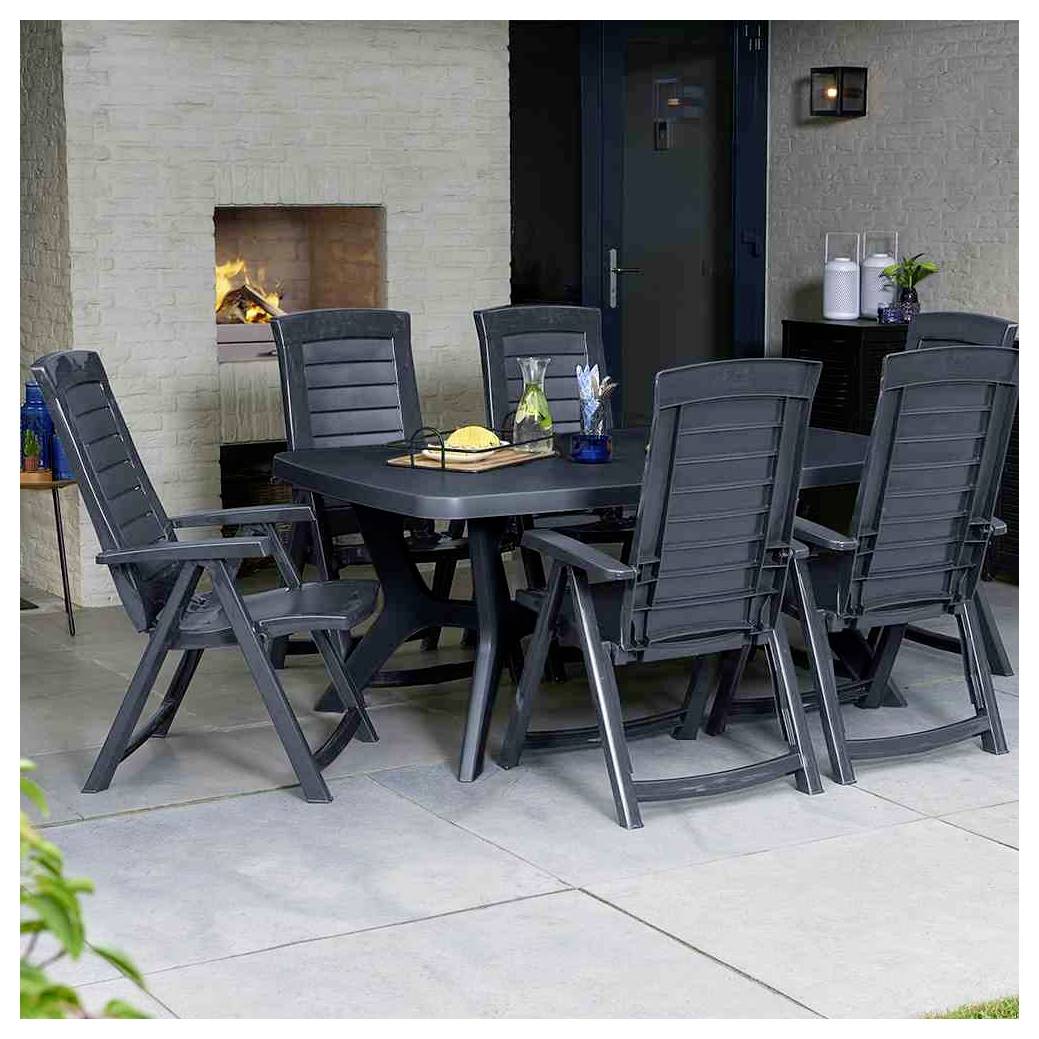 Garnitura za hranjenje na zunanji terasi s šestimi črnimi stoli okrog mize, poleg prižgane kamina in temnih vrat ob sivi steni.