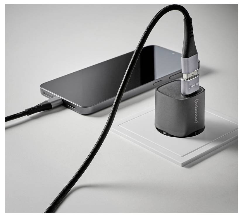 Pametni telefon, ki se polni na mizi preko črnega USB kabla, povezanega s sivo brezžično napajalko.