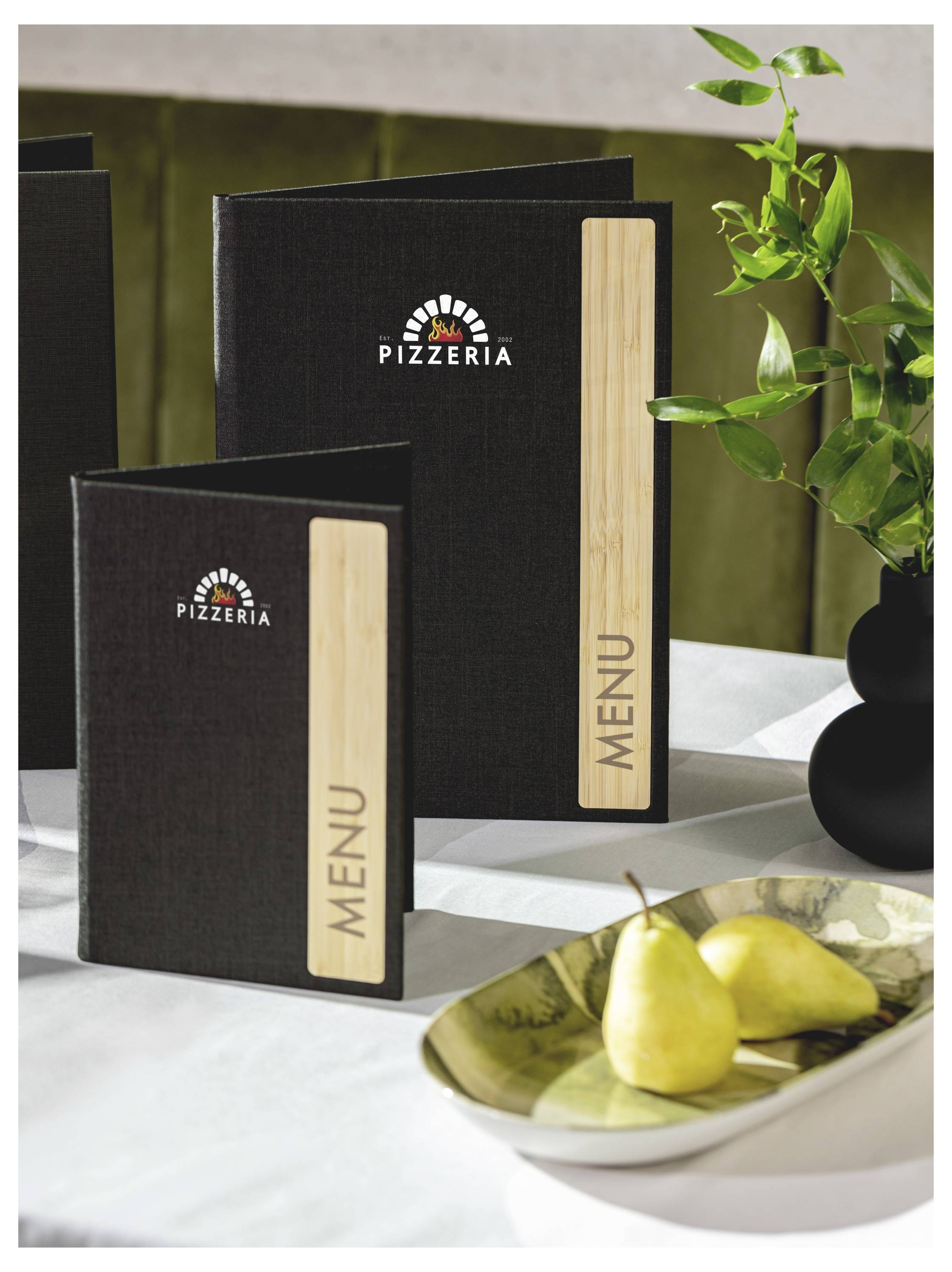 Dve črni mapi s pizzerije z lesenimi ploščami 'MENU' stojita na mizi poleg vaze s zelenimi listi in sklede hrušk.