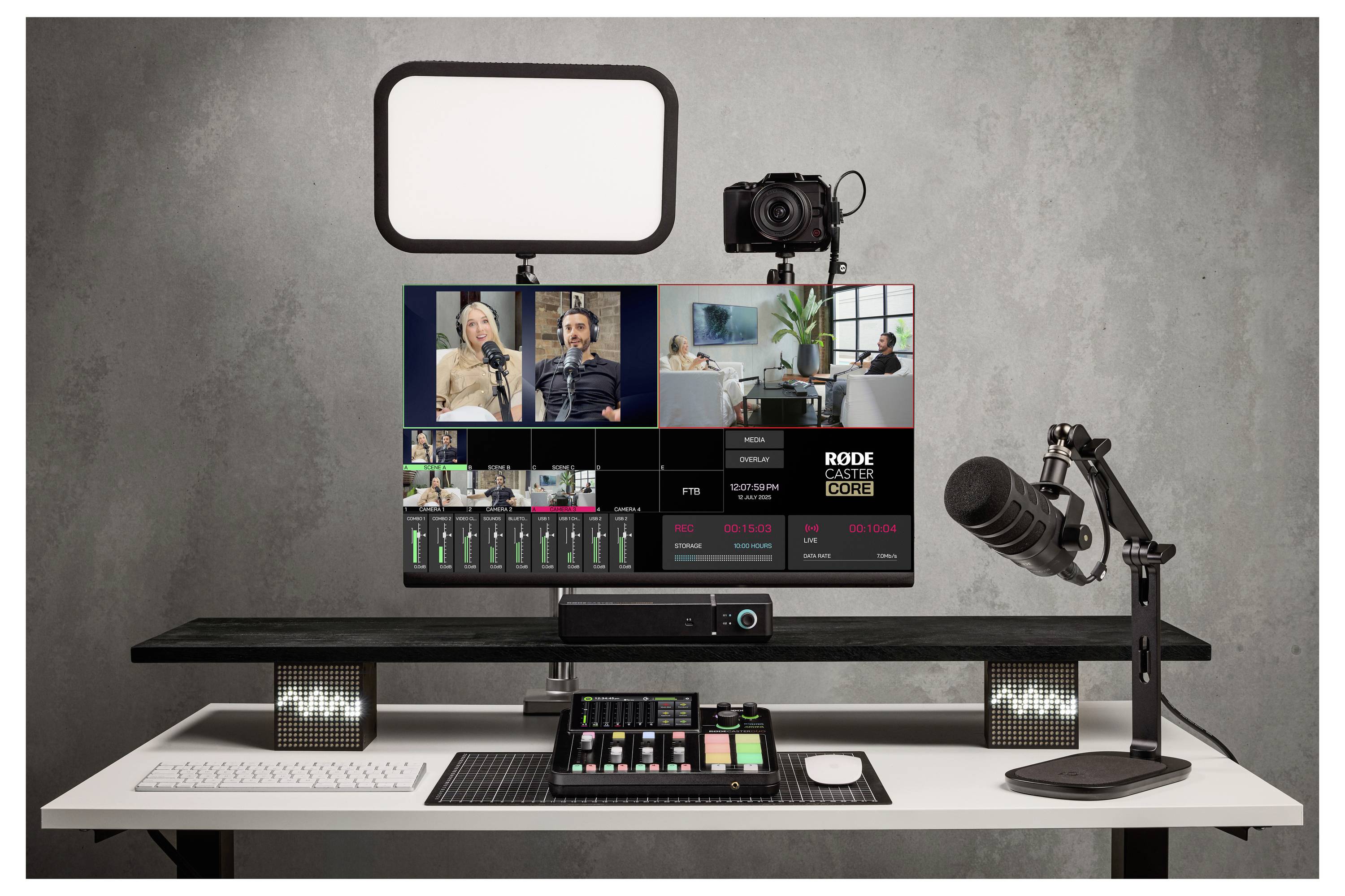 Namestitev za proizvodnjo podkasta/videov z monitorjem, ki prikazuje snemanje intervjuja z več kamerami, obročno lučjo, kamero, mikrofonom, mešalnikom in tipkovnico na mizi.