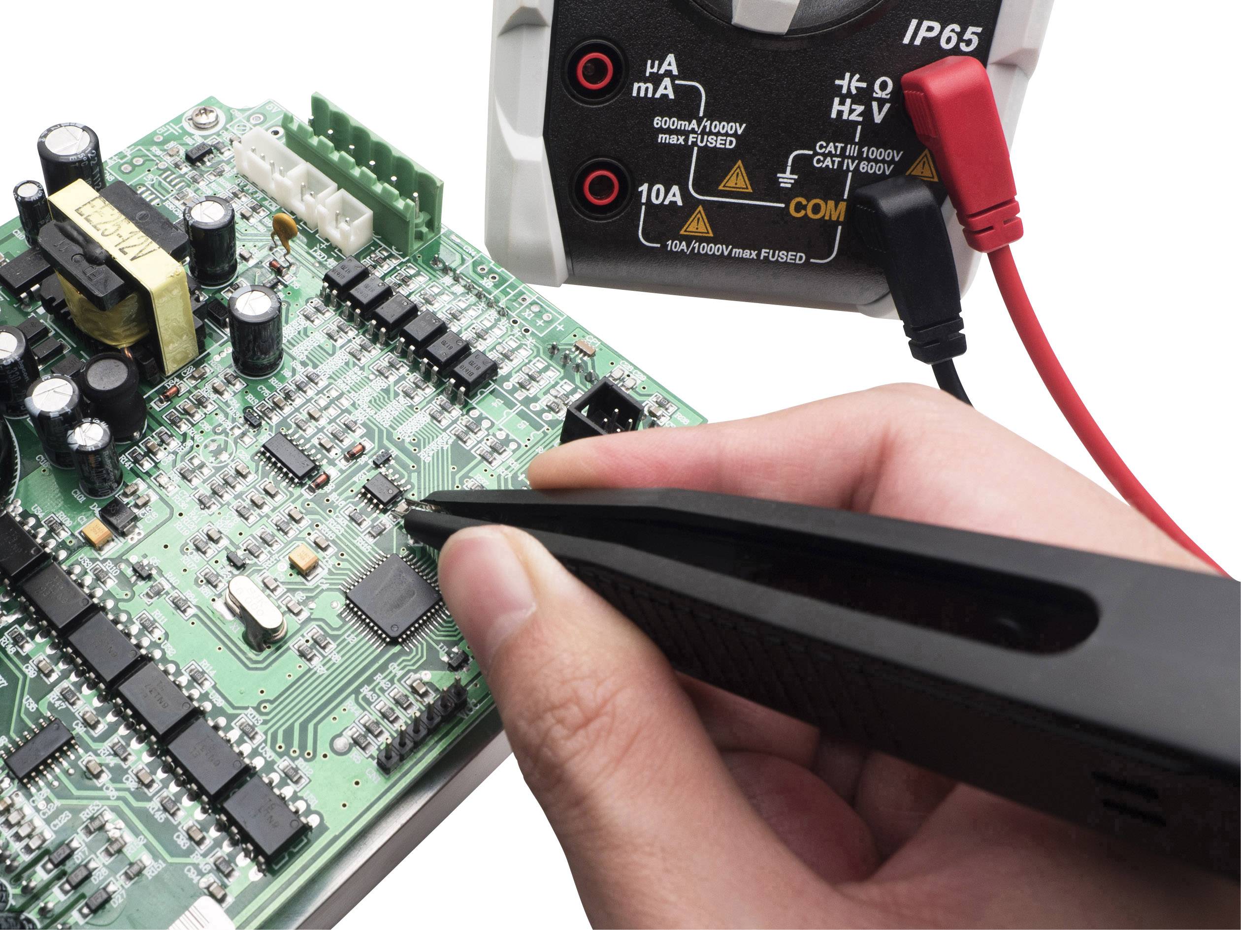 Roka drži merilno napravo na tiskanem vezju. Ozadje prikazuje IP65-enkapsuliran preizkuševalni instrument. Teme: elektronika, meritve, testiranje.