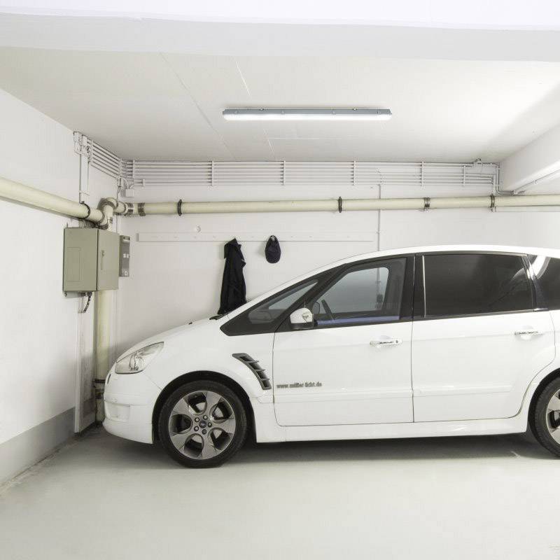 Belo avtomobil stoji v prazni garaži. Na steni visita dva kljuka. Zgoraj je pritrjena fluorescenčna cev.