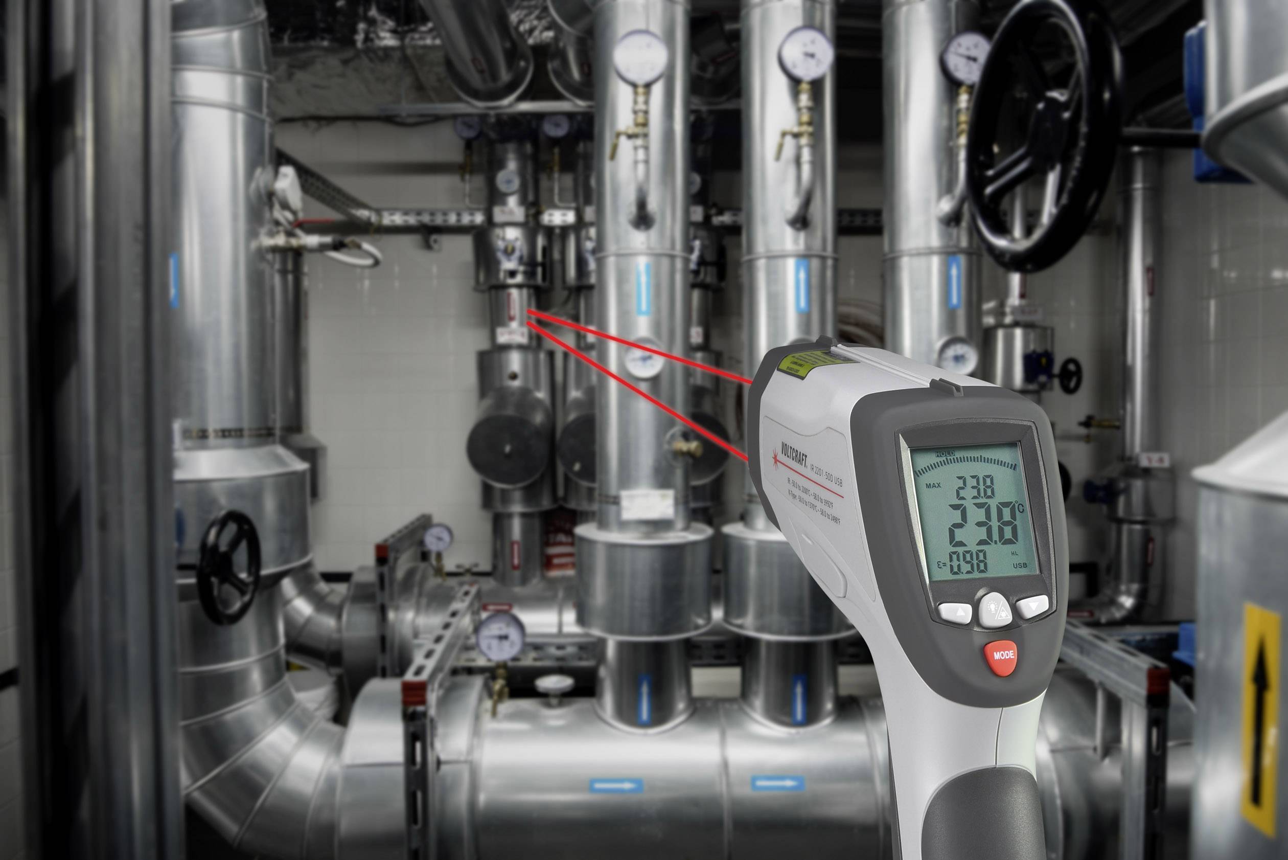 Digitalni infrardečo termometer kaže -23,8°C in usmerja rdeč laser na cevi v industrijskem prostoru naprave.