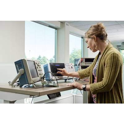 Oseba dela za mizo z več elektronskimi merilnimi napravami. Zavrti gumb enega izmed naprav, da bi opravila nastavitve.
