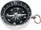 Okrogel kompas s črno številčnico prikazuje smeri neba. Kazalec kaže proti severu, označen z 'S'.